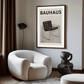 Modern interior with a white armchair, black floor lamp, and 'Bauhaus' poster on the wall.