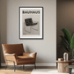Bauhaus poster above a brown leather armchair in a modern living room.